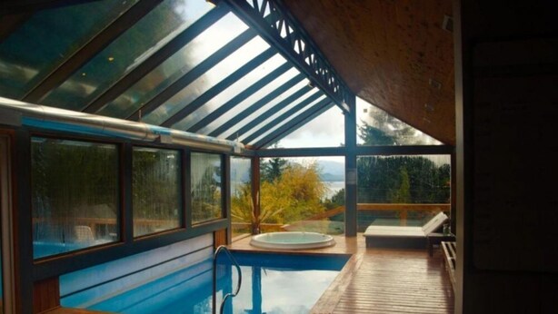 A modern indoor swimming pool with a glass ceiling, wooden deck, and a hot tub. - Impeccable 2BR Condo w Spacious Balcony and Waterfront (San Carlos de Bariloche)