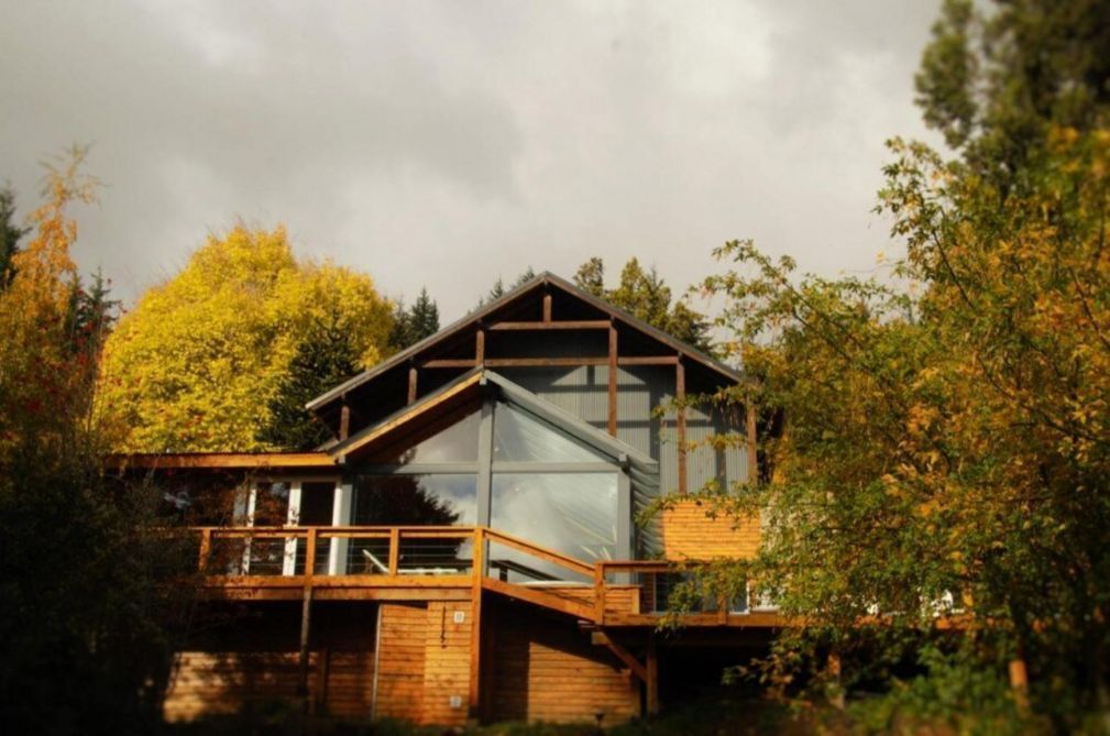Eine Holzhütte mit einer Holzterrasse, großen Fenstern und einem geneigten Dach.