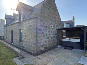 A stone building with a small patio area, a hot tub, and a wooden fence. - Fisherman's Cottage (Fraserburgh)