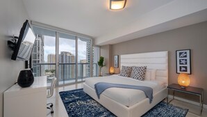 Ein modernes Schlafzimmer mit einem großen Bett, einem Schreibtisch und Blick auf hohe Gebäude.