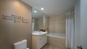 Ein modernes Badezimmer mit Toilette, Waschbecken und Badewanne. Ein Spiegel spiegelt den Raum wider, und eine Wandtafel zeigt Badezimmerartikel.