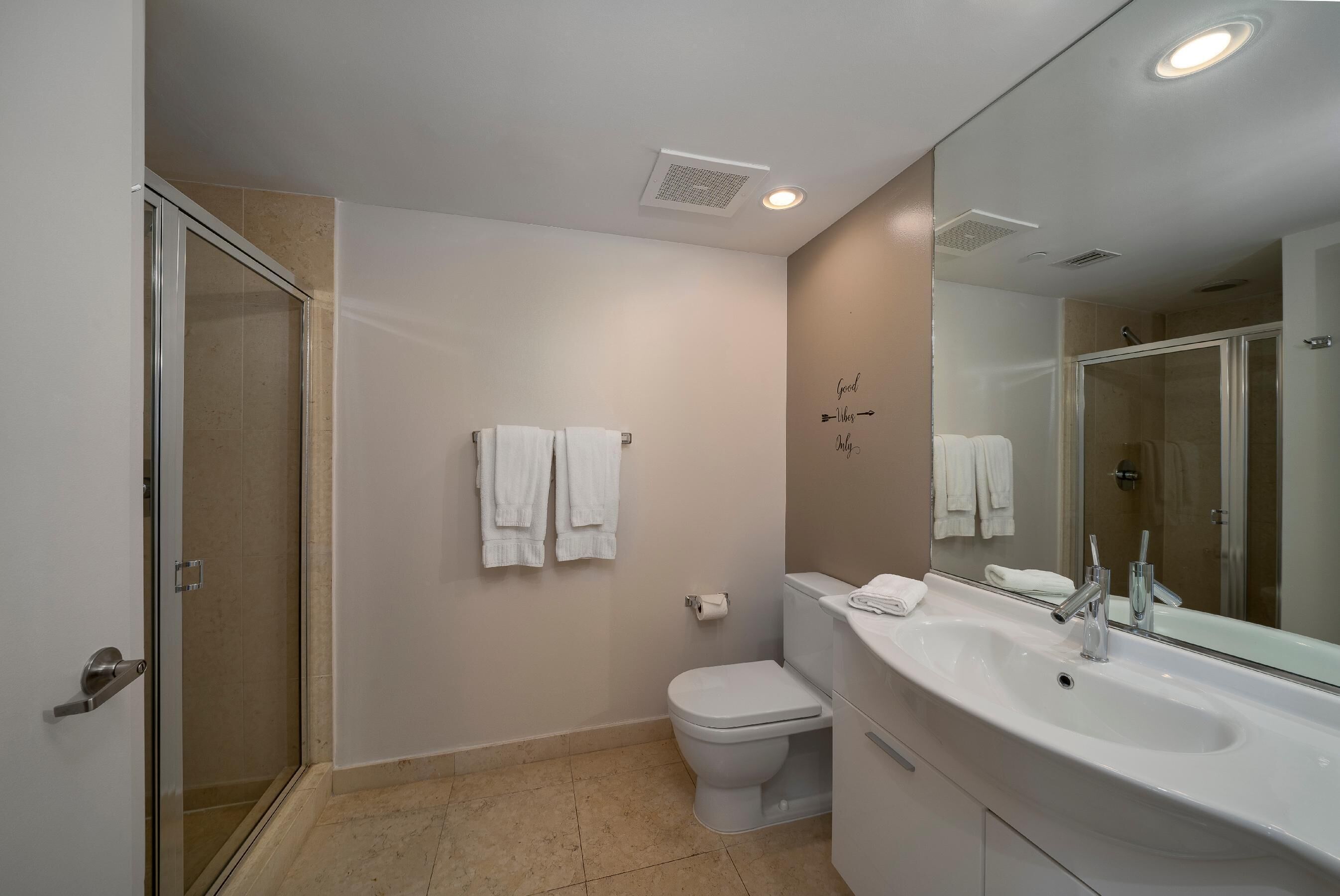 A modern bathroom with a glass shower enclosure, a white toilet, and a large vanity with a mirror.
