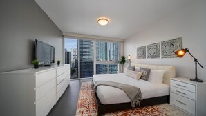 A modern bedroom with a large bed, a TV, a desk, and a view of the city. - Presidential River & City View (Miami)