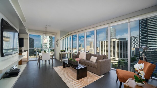 A modern living room with a large window, a sofa, a coffee table, and a TV. - Presidential River & City View (Miami)