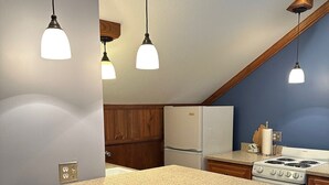 Eine Küche mit einer langen Kochinsel, Holzschränken, einem Kühlschrank, einem Herd und Pendelleuchten.