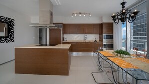 A modern kitchen with a central island, stainless steel appliances, and a dining area with a glass table and chairs. - Presidential Ocean View (Miami)
