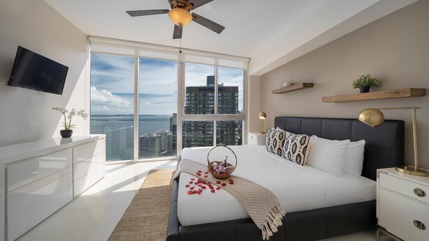 A modern bedroom with a large bed, a ceiling fan, a TV, a city view, and a balcony. - Presidential Ocean View (Miami)
