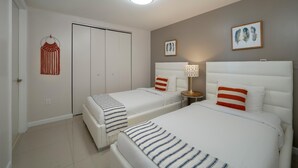 Ein Hotelzimmer mit zwei Betten, einem Nachttisch mit Lampe, einem Wandbild und einer Wandweberei aus Fransen.