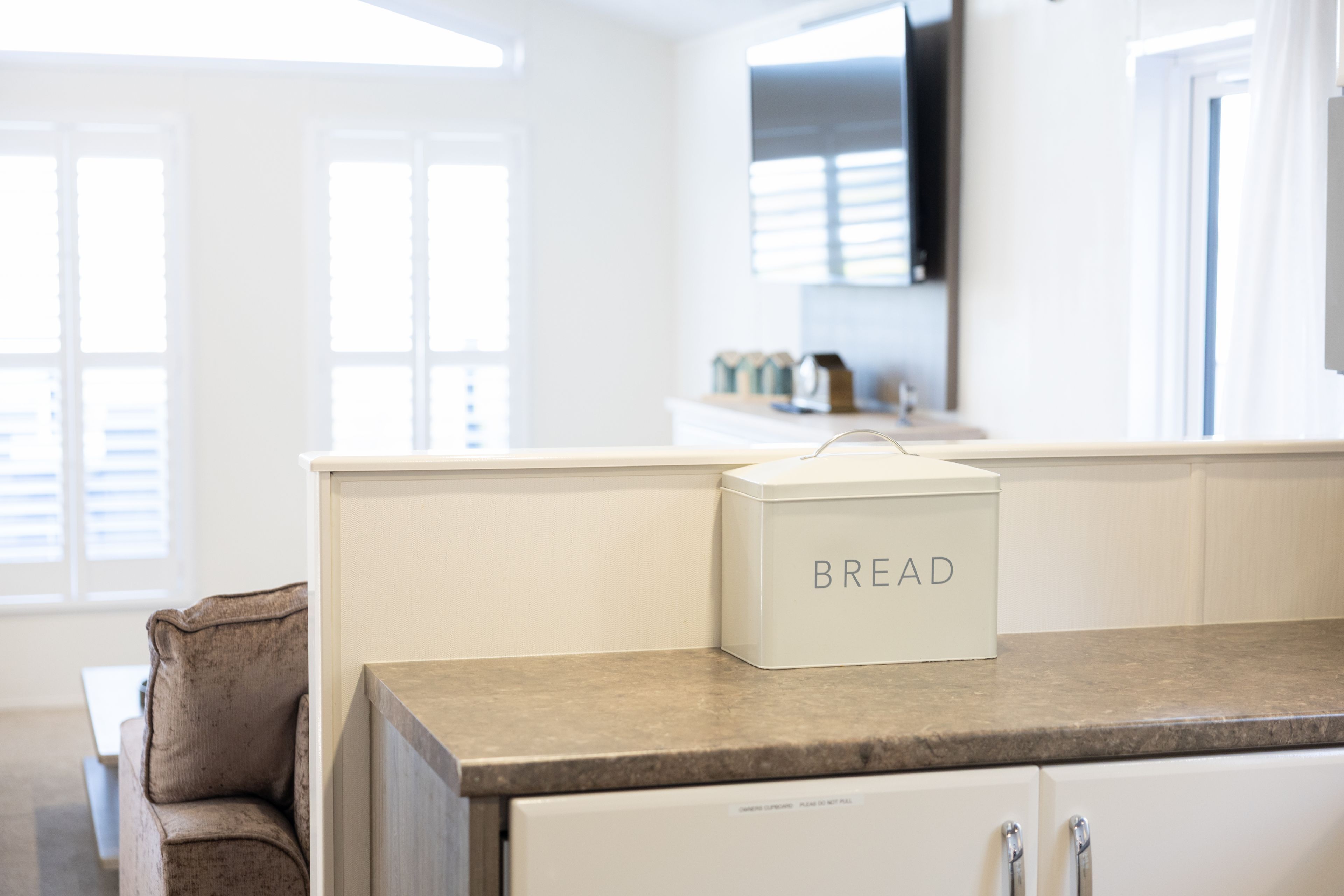 A kitchen with a countertop, a white box labeled 'BREAD,' and a brown chair.