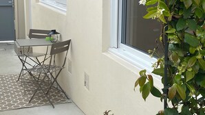 Een klein terras met een tafel en stoelen, een bloempot en een raam met uitzicht op een gebouw.