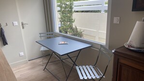 Een klein balkon met een tafel en stoelen, uitzicht op een witte schutting en groen, en een houten kast.