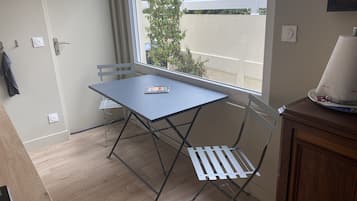 Un petit balcon avec une table et des chaises, une vue sur une clôture blanche et sur la verdure, ainsi qu’un meuble en bois.