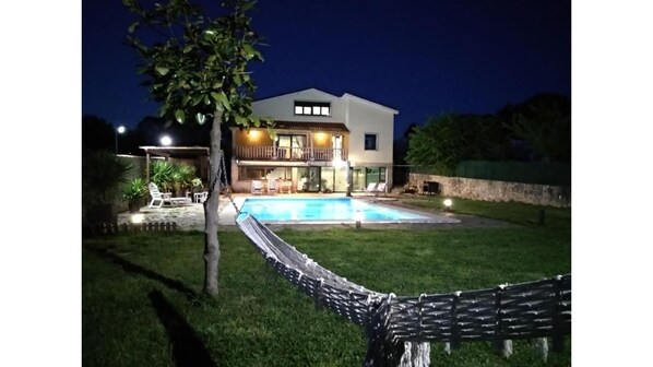 A two-story house with a swimming pool, a hammock, and outdoor seating.
