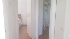 Un estrecho pasillo con suelo de madera, paredes blancas y una puerta que da a un dormitorio con cama y cómoda.