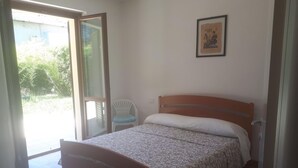 Une chambre à coucher avec un lit en bois, une chaise, une porte donnant sur un balcon et un tableau encadré au mur.