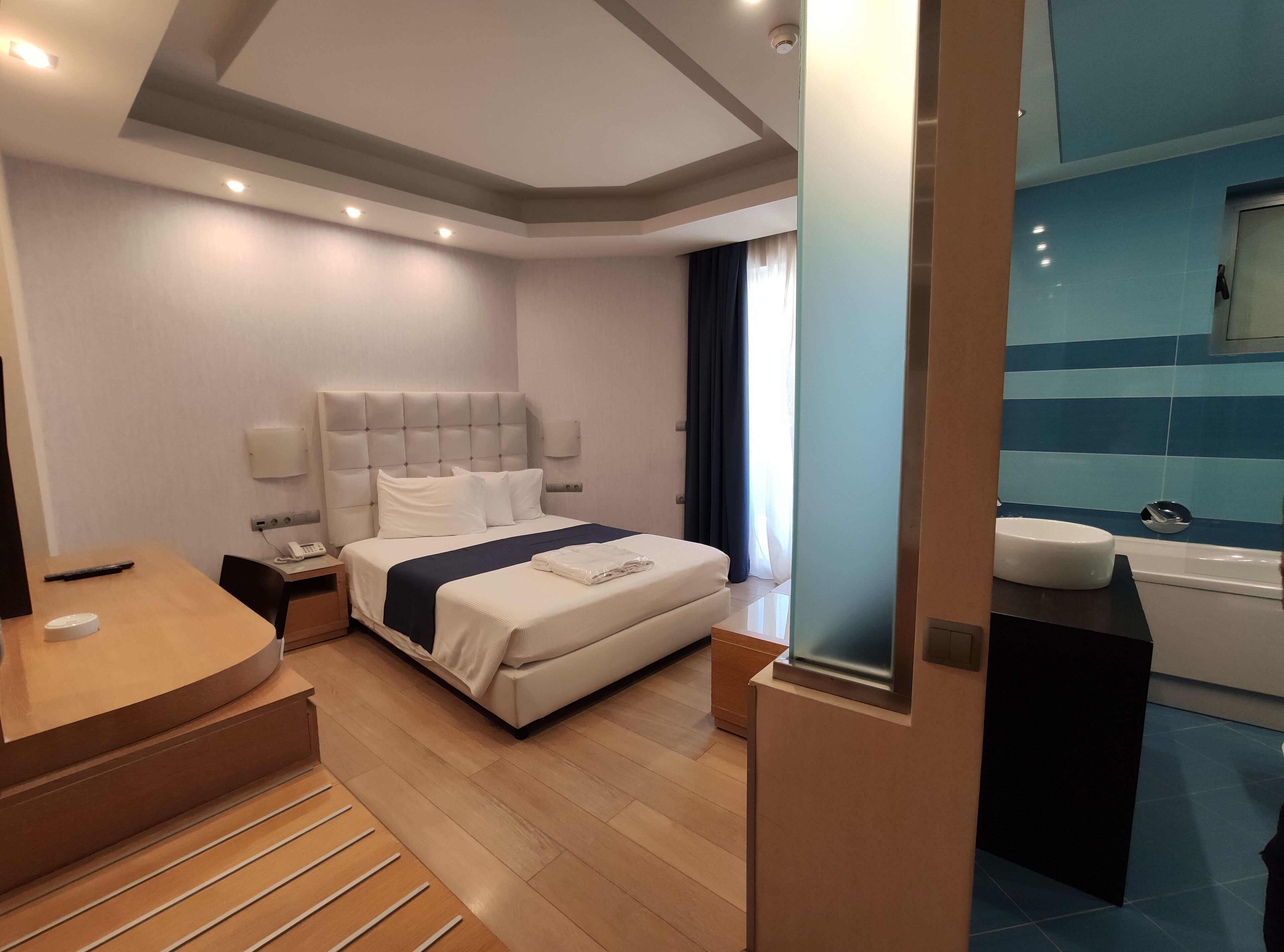 Habitació d'hotel moderna amb un llit gran, taules de nit, escriptori i un bany amb banyera i rentapans.