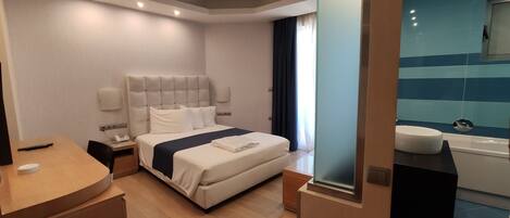Una habitación de hotel moderna con una cama grande, mesitas de noche, un escritorio y un baño con bañera y lavabo.