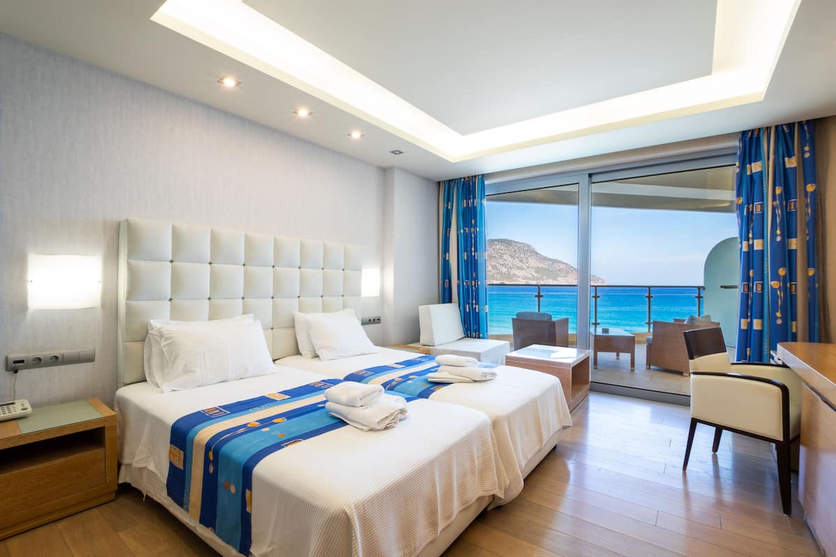 A hotel room with a large bed, a desk, a chair, and a view of the sea.