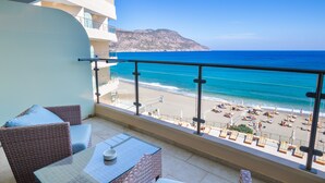 A balcony with wicker furniture, a glass table, and a view of the beach and ocean. - Konstantinos Palace (Karpathos)