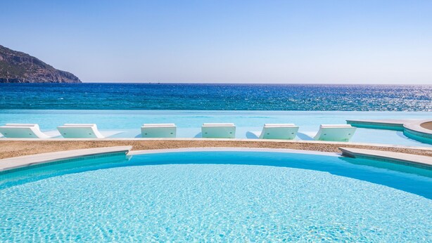 A clear blue pool with lounge chairs and a view of the sea. - Konstantinos Palace (Karpathos)