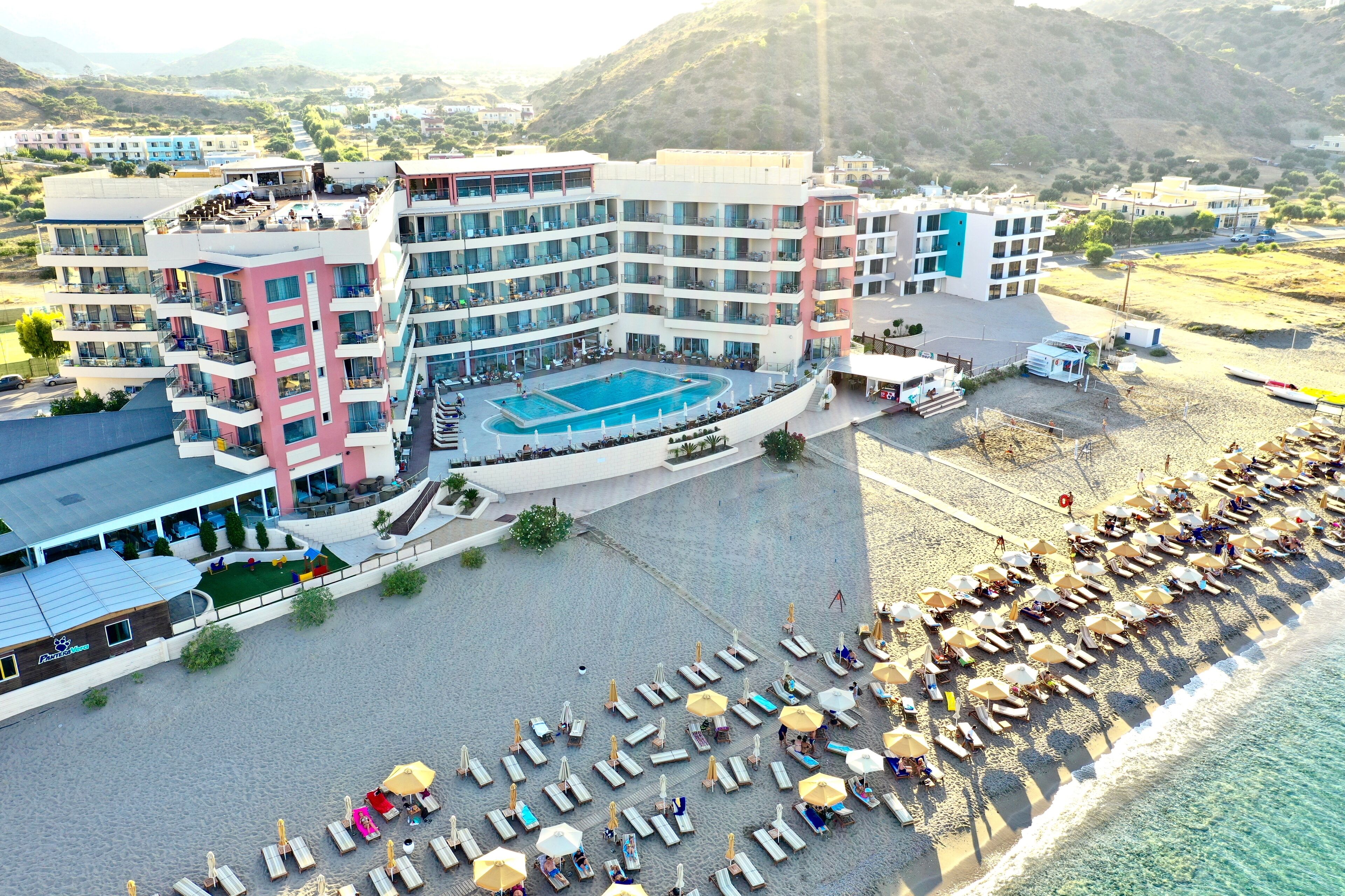 Un hotel con varias plantas, piscina y zona de playa con tumbonas y sombrillas.