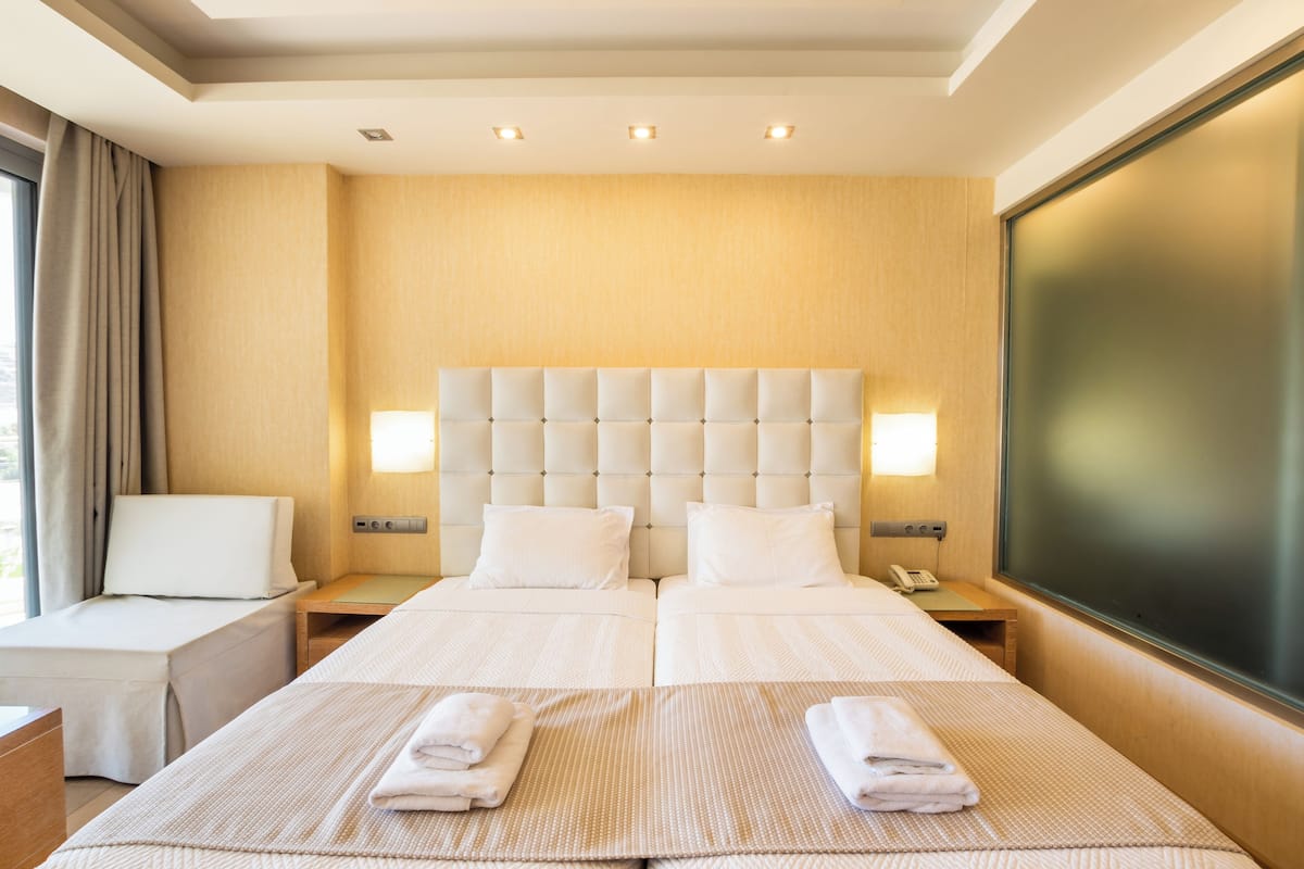 A hotel room with a large bed, two bedside tables, a desk, and a large window.