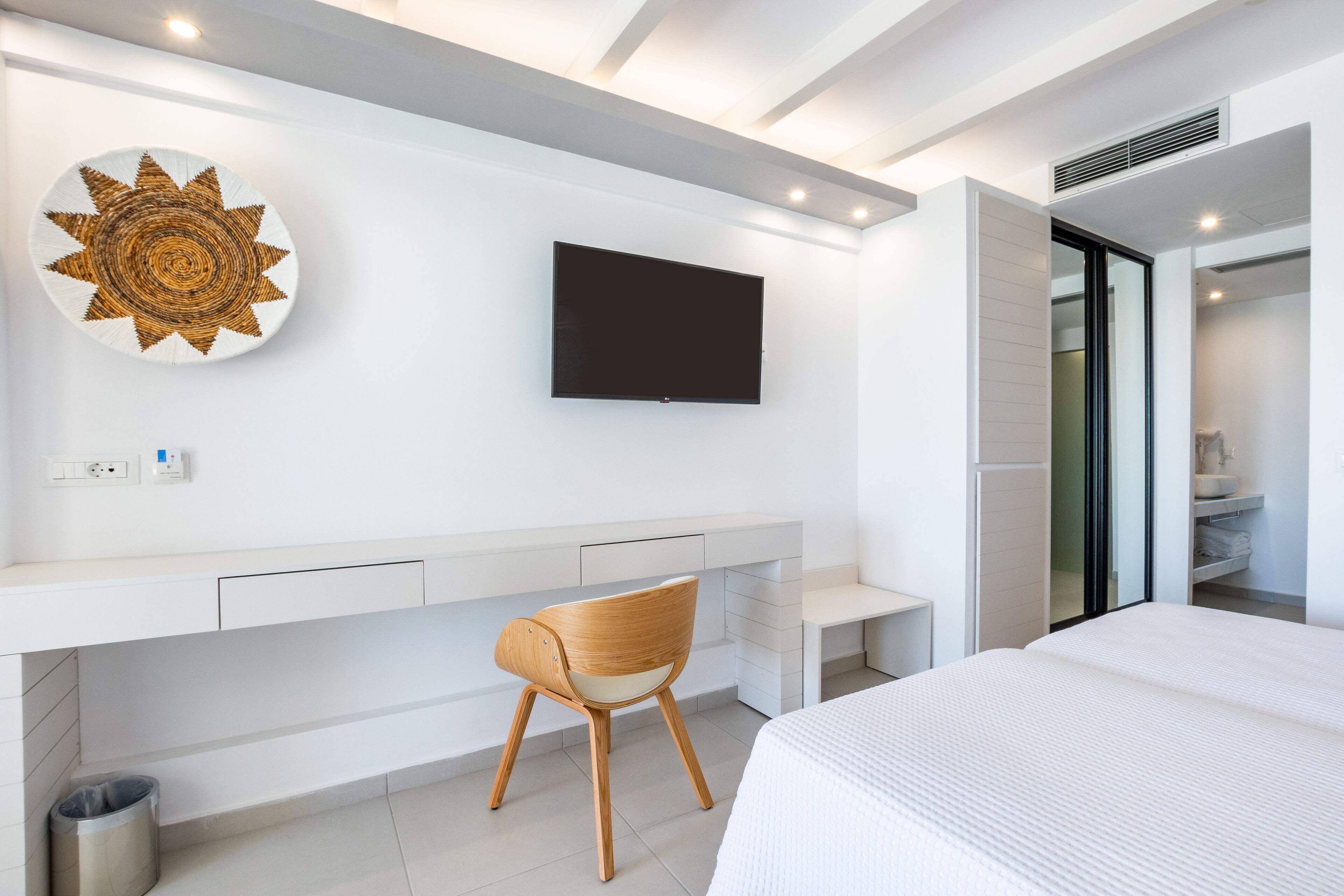 A modern hotel room with a large bed, a desk with a chair, a flat-screen TV, and a decorative wall piece.
