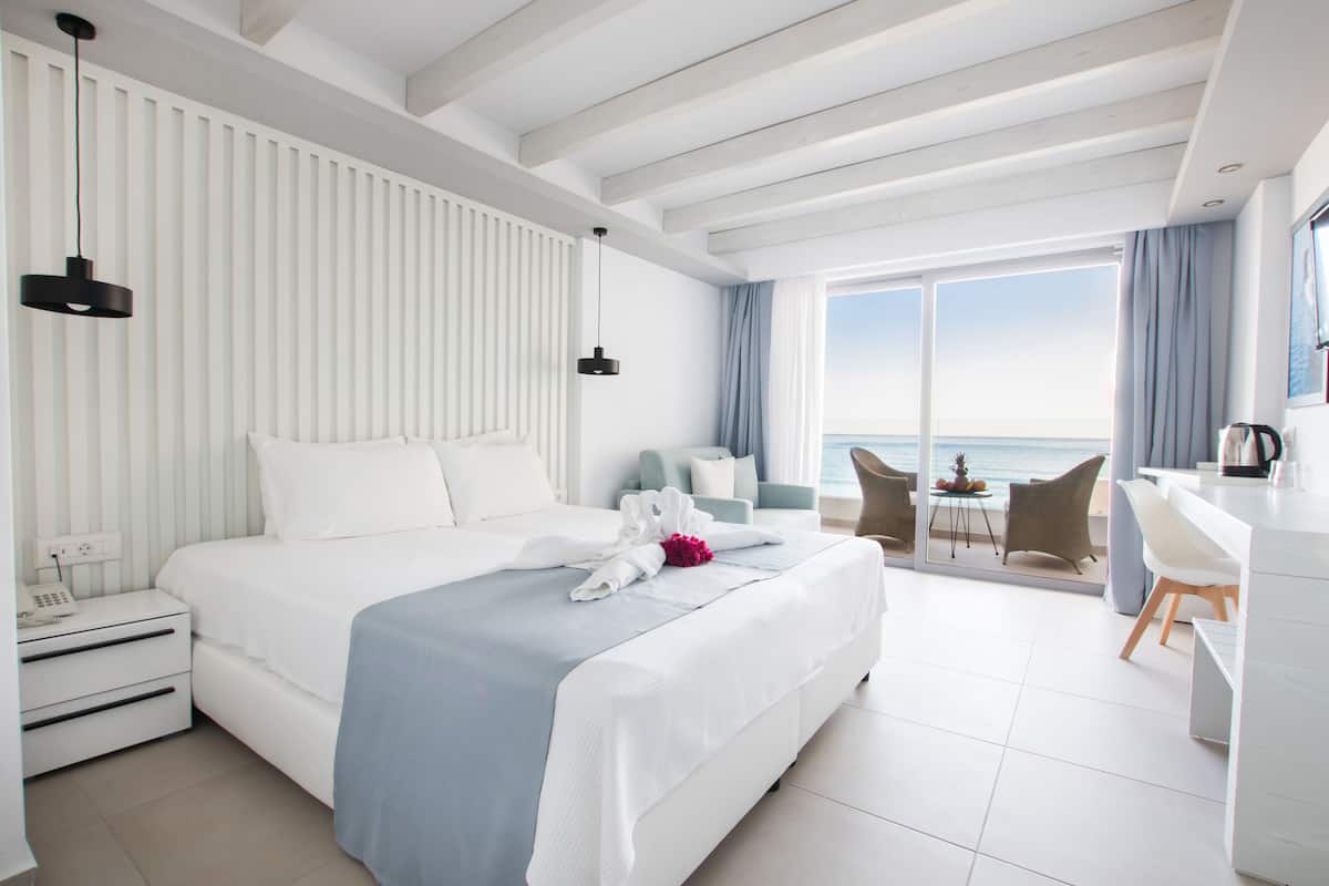 A modern hotel room with a large bed, a desk, and a view of the sea.