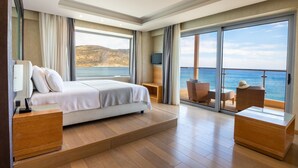 A modern bedroom with a large bed, a TV, and a balcony with a view of the sea. - Konstantinos Palace (Karpathos)