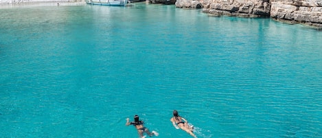 A clear turquoise sea with rocky cliffs and a boat in the background.