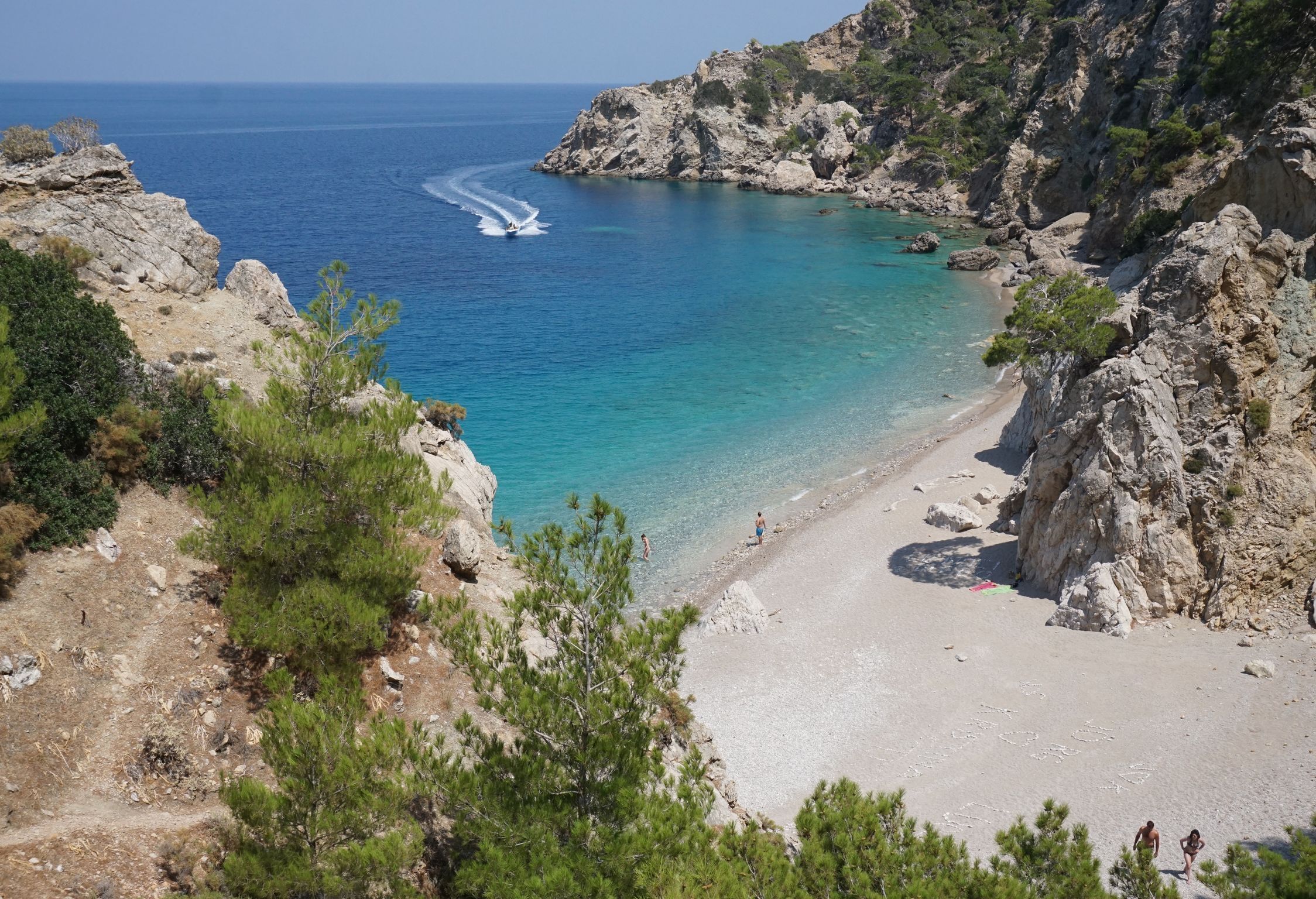A coastal beach with rocky cliffs, clear turquoise waters, and a sandy shore.