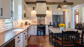 A kitchen with white cabinets, a wooden ceiling, a central island with a sink, and a dining area with a table and chairs. - Welcome to A Little Bit O' Heaven! (Lake Toxaway)