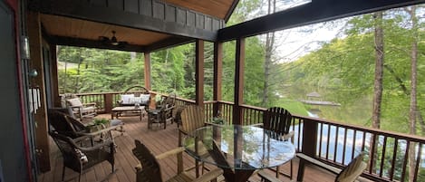 Een houten terras met een glazen tafel en stoelen, met uitzicht op een meer en bos.