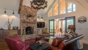 A spacious living room with a stone fireplace, leather furniture, and large windows. - Welcome to A Little Bit O' Heaven! (Lake Toxaway)