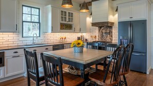 A kitchen with white cabinets, a central island with chairs, a refrigerator, and hanging pendant lights. - Welcome to A Little Bit O' Heaven! (Lake Toxaway)