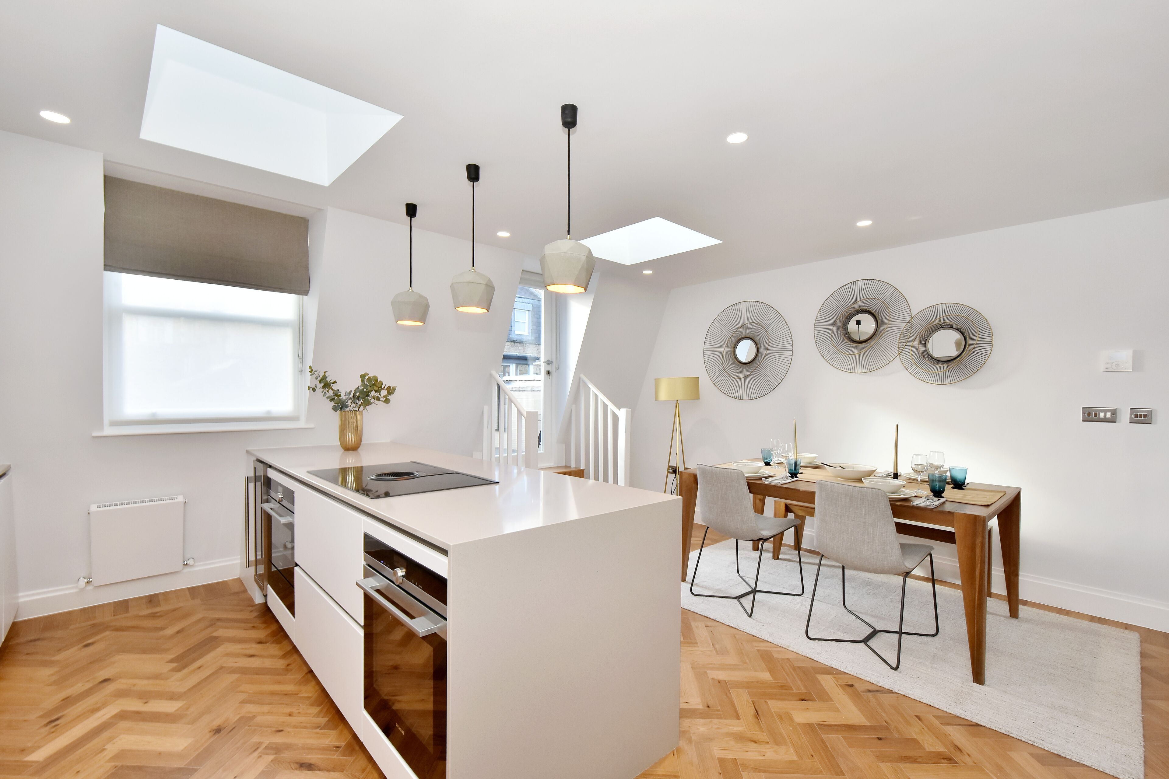 A modern kitchen with a central island, pendant lighting, and a dining area with a wooden table and chairs.