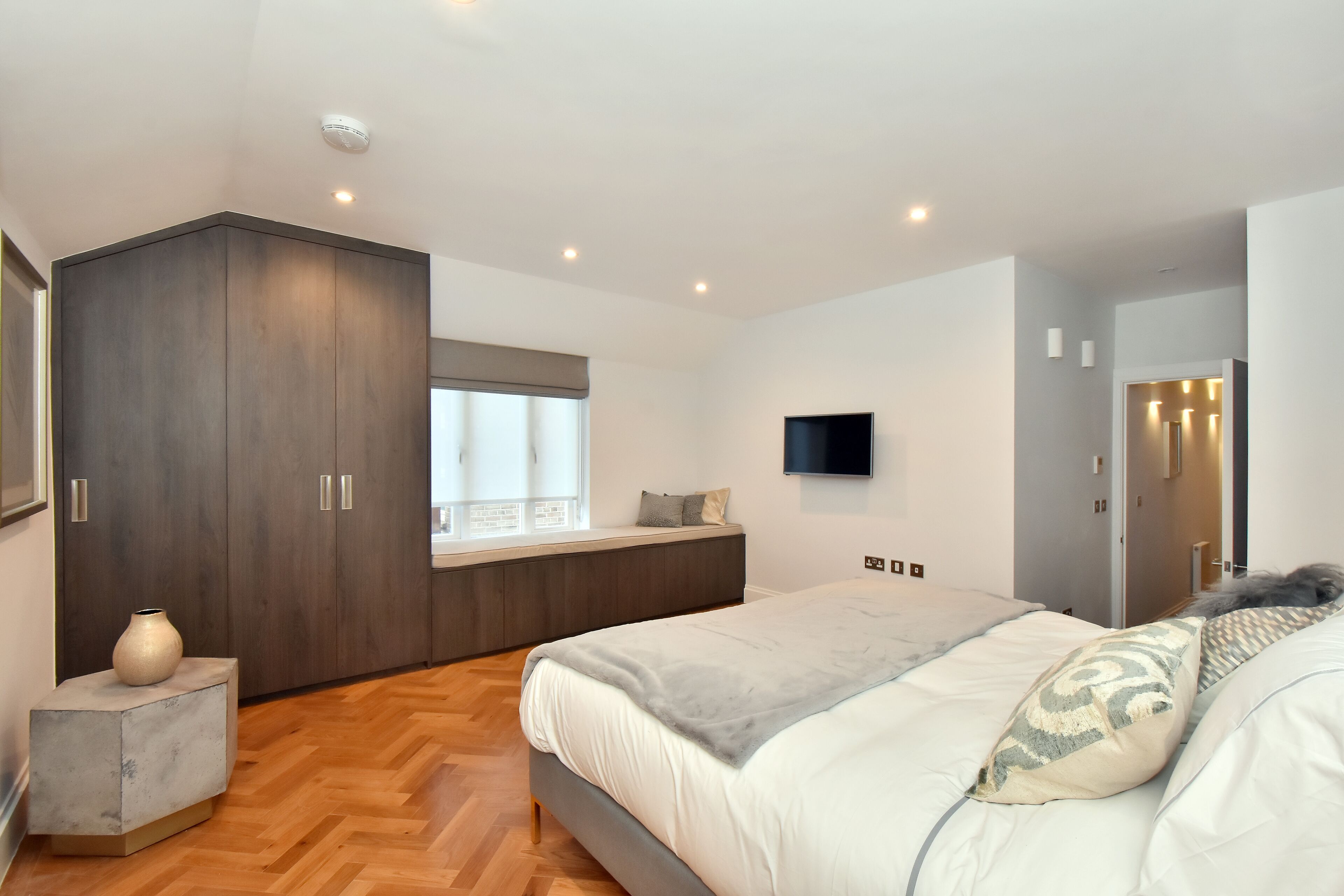 A modern bedroom with a large bed, a built-in wardrobe, a flat-screen TV, and a window with a view.