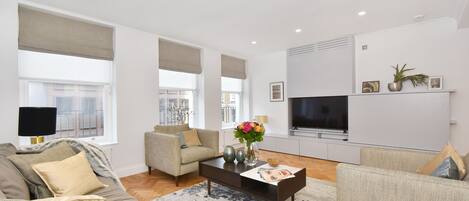 A modern living room with a sofa, armchairs, a coffee table, and a TV.