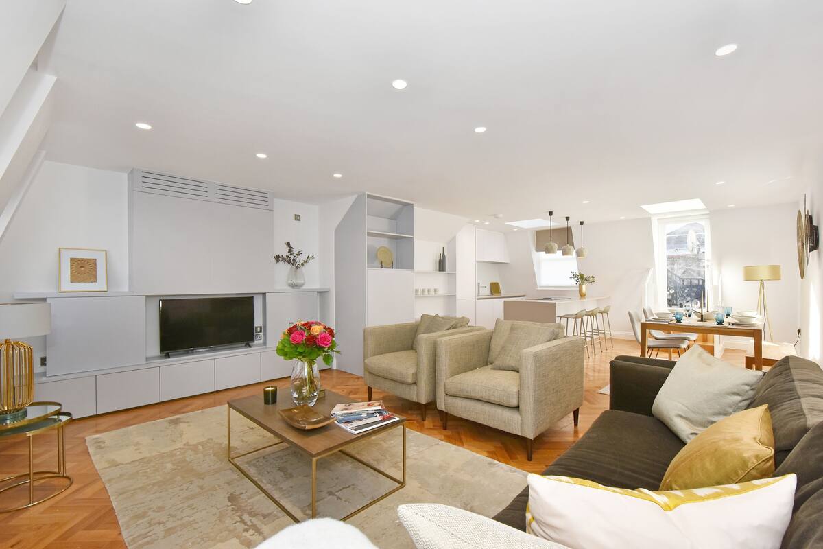 A modern living room with a flat-screen TV, two sofas, a coffee table, and a dining area with a table and chairs.