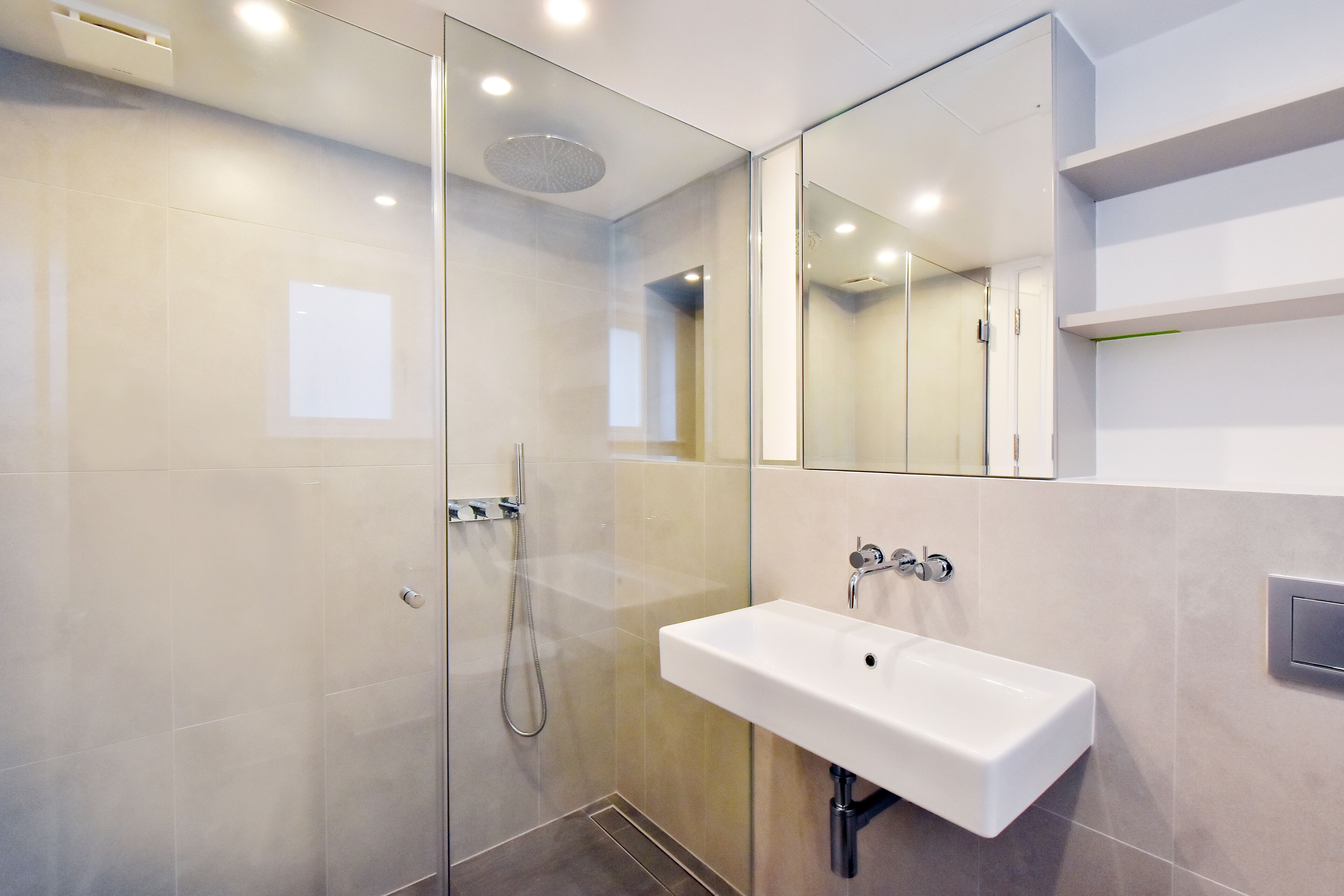 A modern bathroom with a glass-enclosed shower, a white sink, and a large mirror.