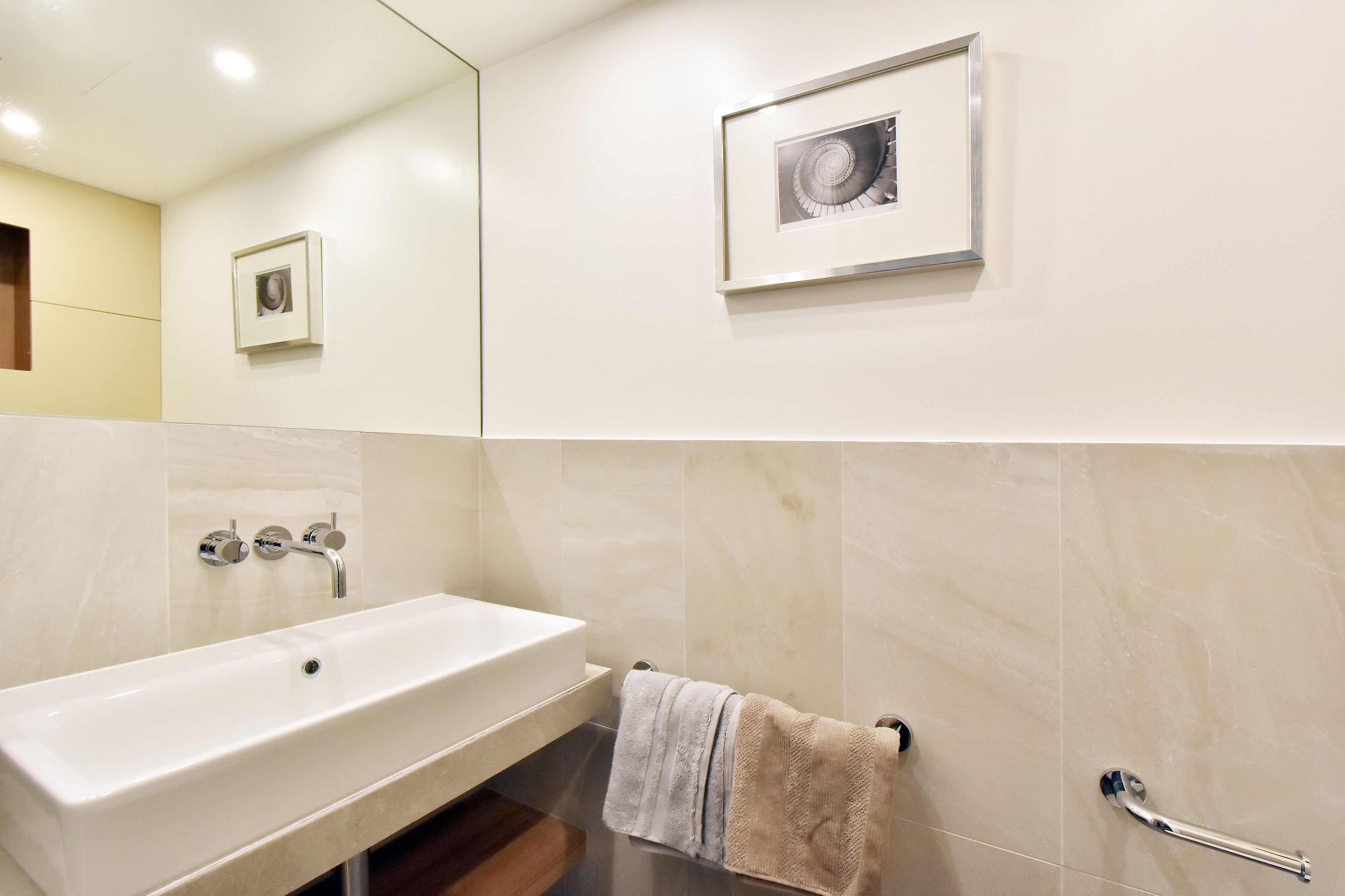 A modern bathroom with a white sink, a mirror, and a framed picture on the wall.