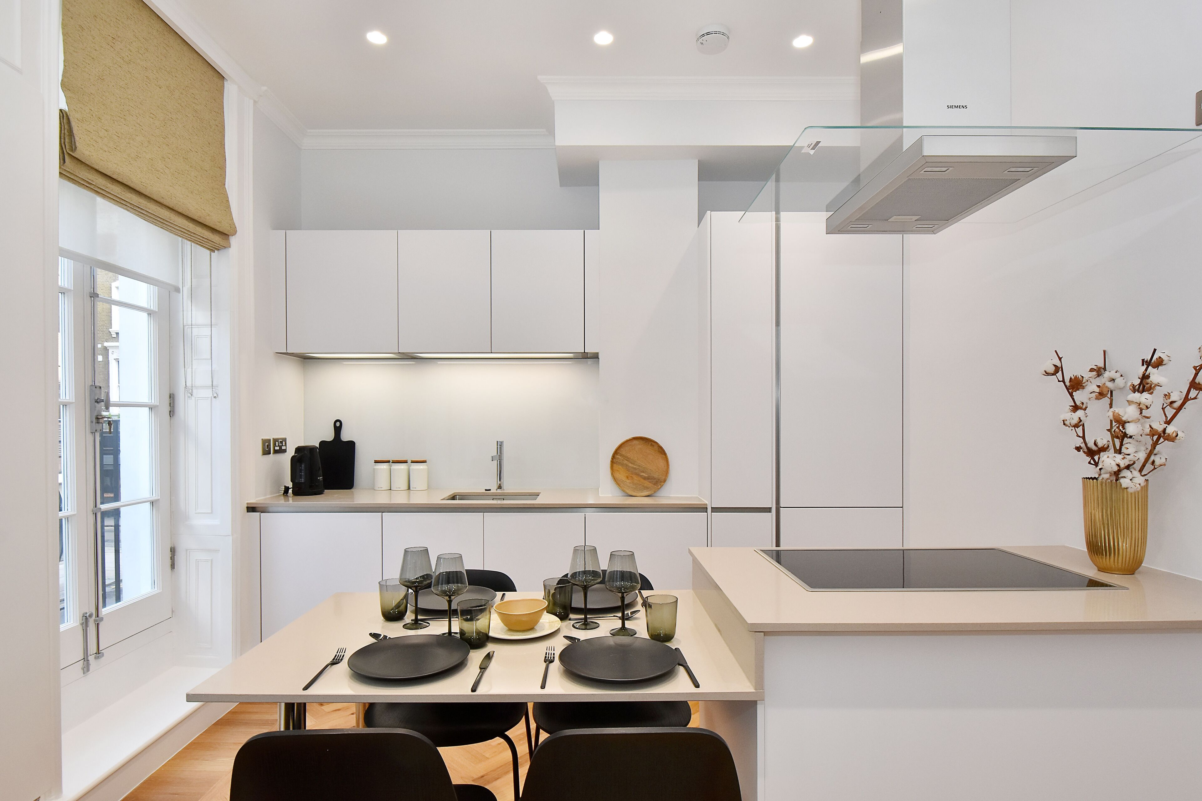 A modern kitchen with white cabinetry, a dining table set with plates, glasses, and cutlery, and a vase with flowers on the island.