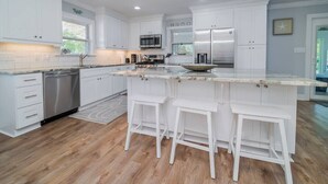 Una cocina moderna con armarios blancos, electrodomésticos de acero inoxidable, una isla grande con taburetes y suelo de madera.