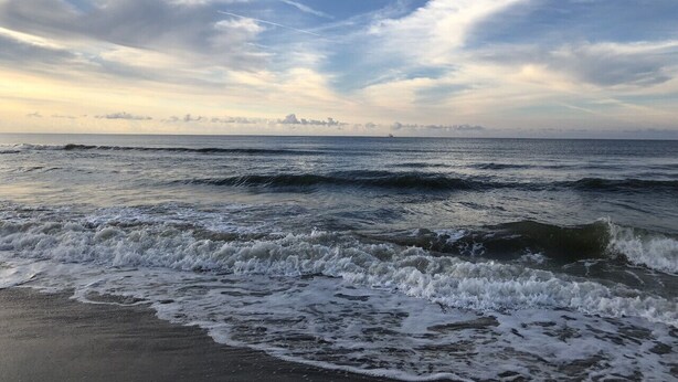 Una playa con olas y cielo nublado.