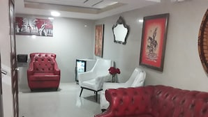 A living room with a red leather sofa, a white armchair, and a red armchair. There is a television and a vase with red flowers on a table. - Hotel Royal Durán (Duran)