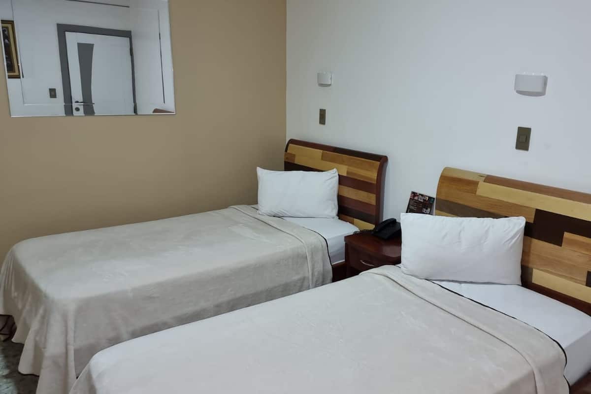 Ein Hotelzimmer mit zwei Einzelbetten, jeweils mit Holz Kopfteil, weißer Bettwäsche und Nachttischen mit Lampen.