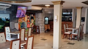 A dining area with wooden tables and chairs, a stone wall with artwork, and a ceiling with patterned tiles. - Hotel Royal Durán (Duran)