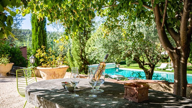 A stone table with wine glasses and a bottle, surrounded by potted plants and a pool. - Independent apartment of two bedrooms of high standing and comfort. (Salernes)