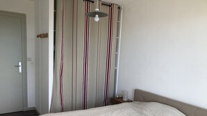 A bedroom with a bed, a curtain with vertical stripes, a bedside table with a lamp, and a door.