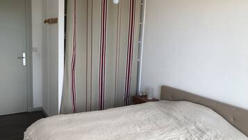 A bedroom with a bed, a curtain with vertical stripes, a bedside table with a lamp, and a door.